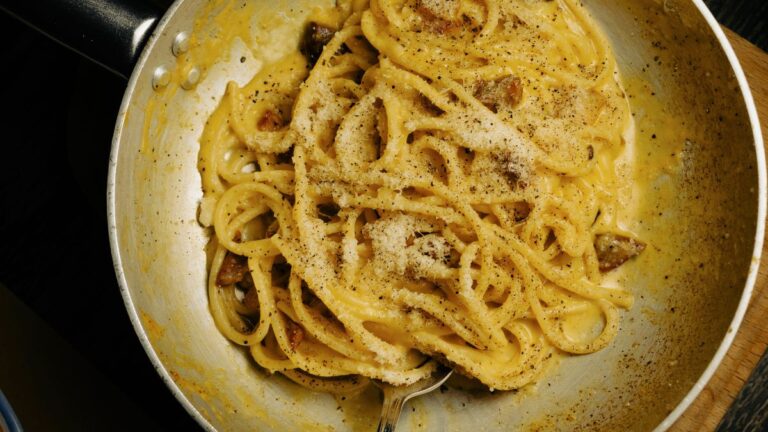 Un piatto di spaghetti alla carbonara fumanti con guanciale croccante e pepe nero